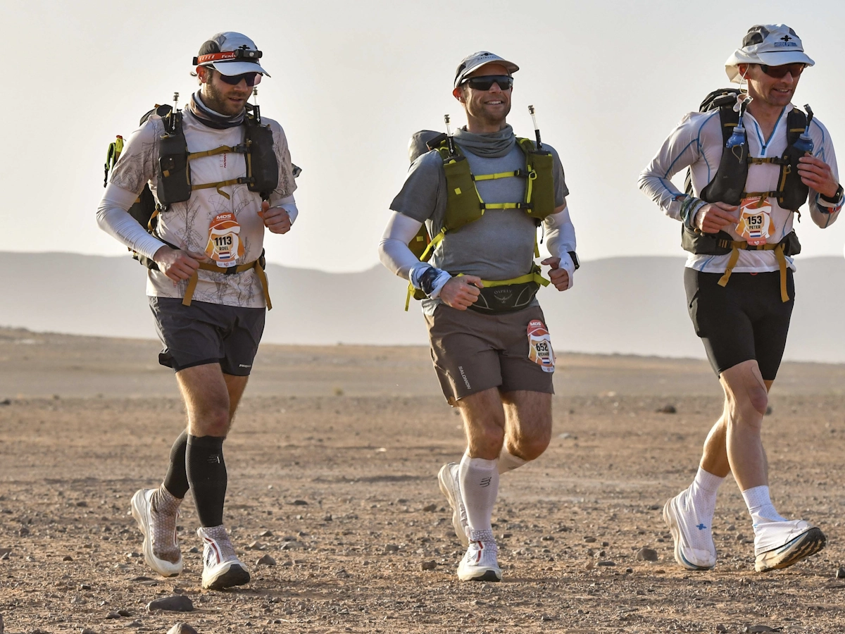 Drie deelnemers lopen samen door het zand tijdens de Marathon des Sables