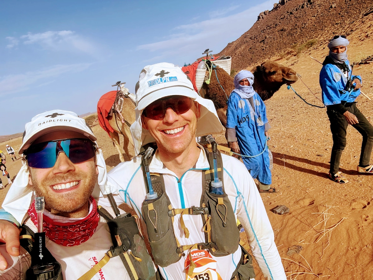 Lopers met kamelen op achtergrond tijdens Marathon des Sables