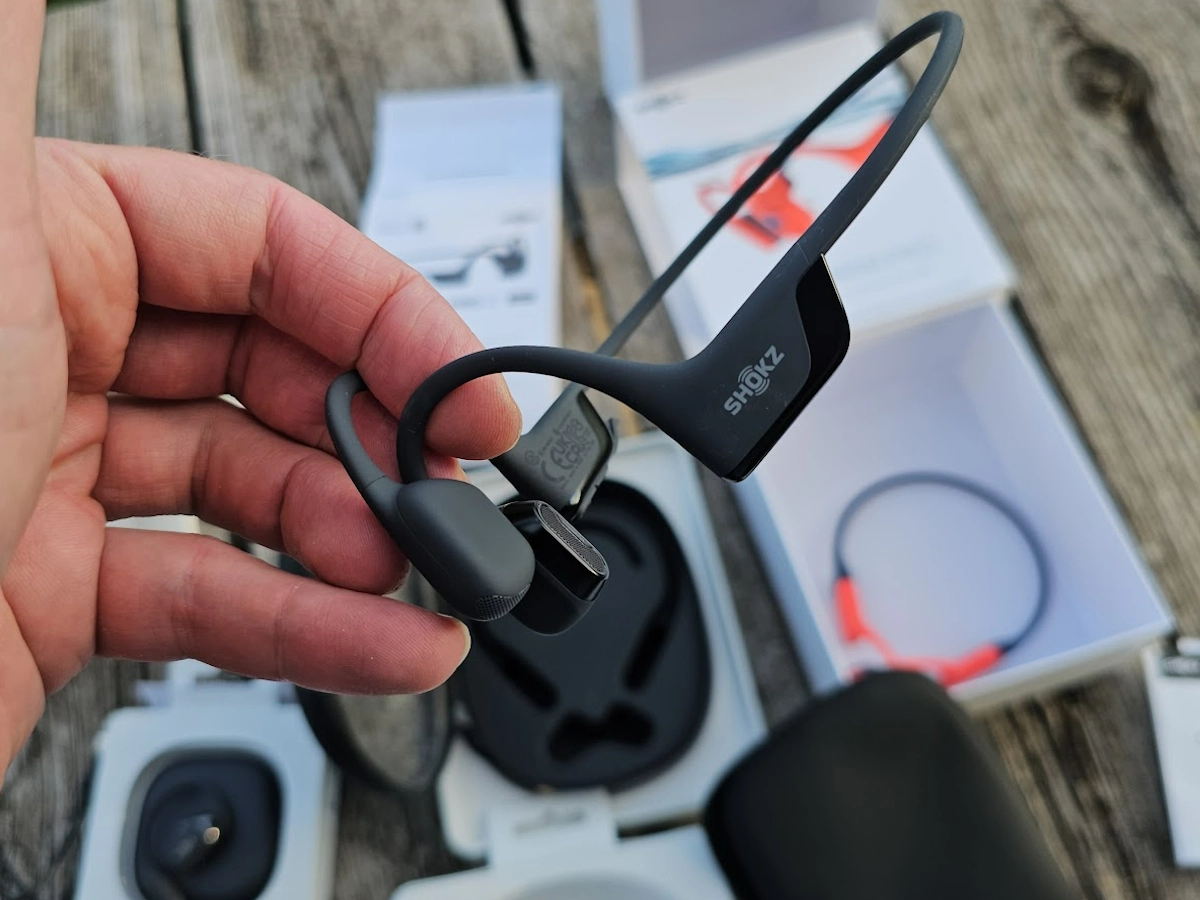 Shokz OpenRun PRO 2, OpenFit 2 en Open Swim Pro met doos op hand