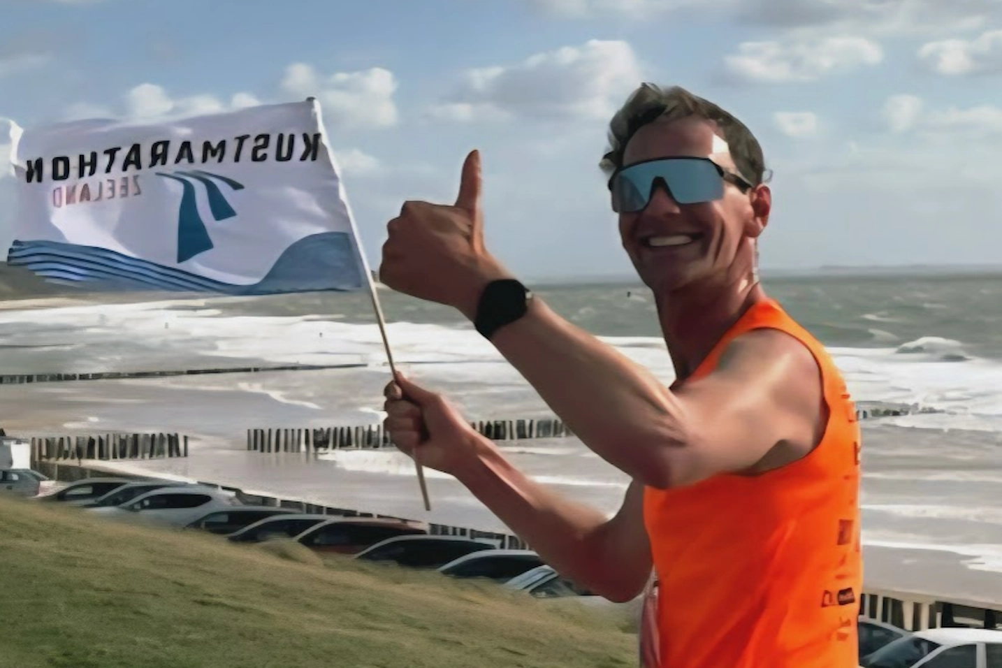 Peter met vlag bij de finish van de stormachtige Kustmarathon Zeeland