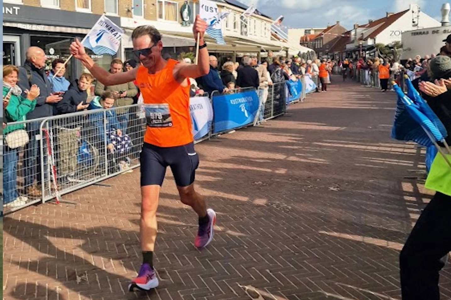 Peter loopt door de finishvlaggen bij harde wind tijdens de Kustmarathon Zeeland